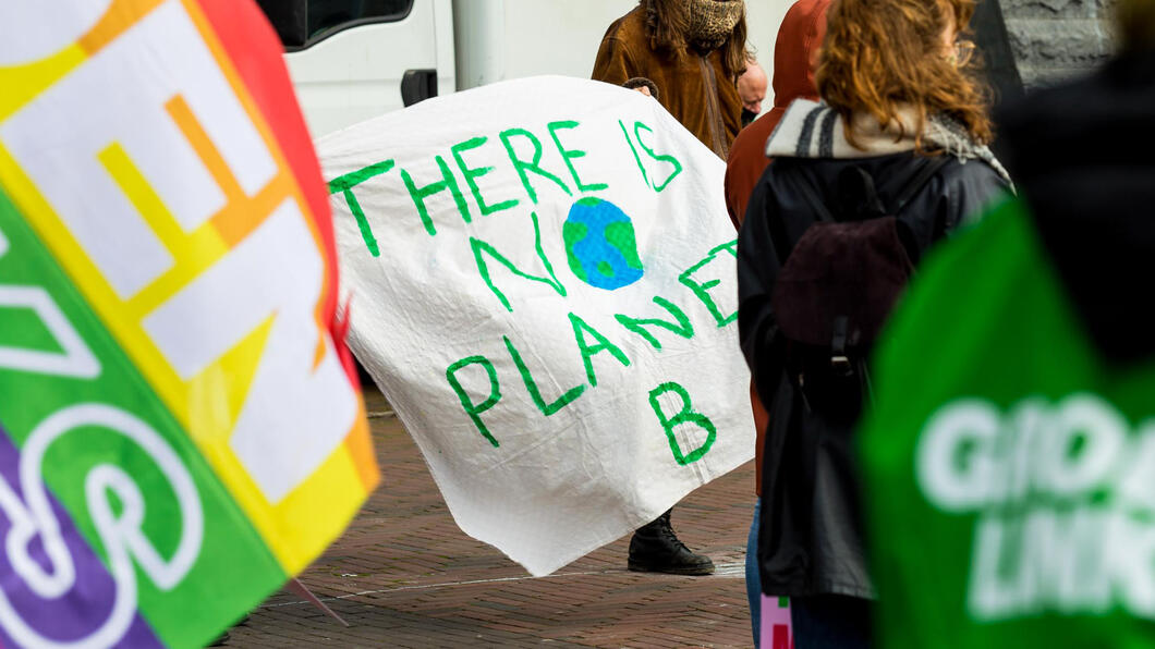 Beeld van spandoek met 'there is no planet B', een GroenLinks regenboogvlag en een iemand met een GroenLinks jasje aan