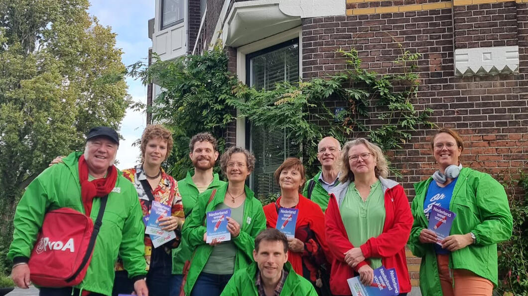Groep vrijwilligers met rode en groene jasjes met flyers in hun handen