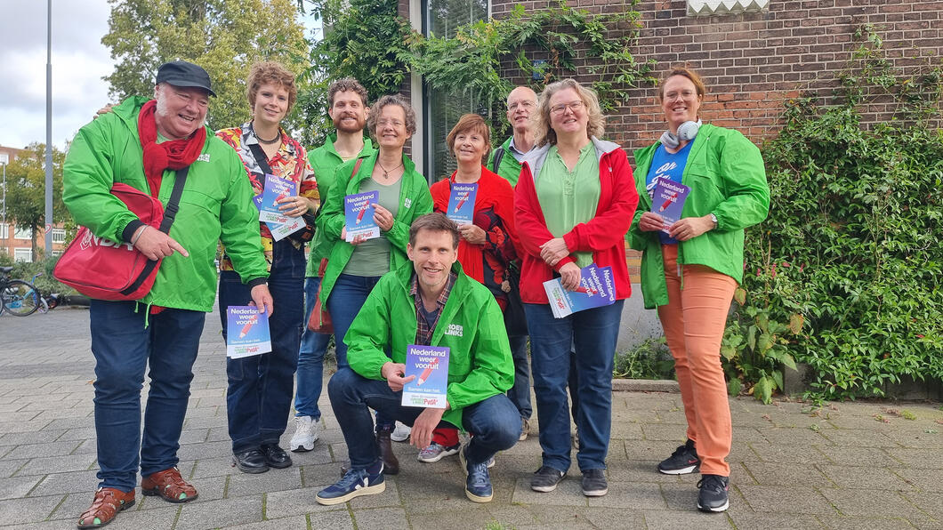 Groep vrijwilligers met rode en groene hesjes met flyers in hun handen