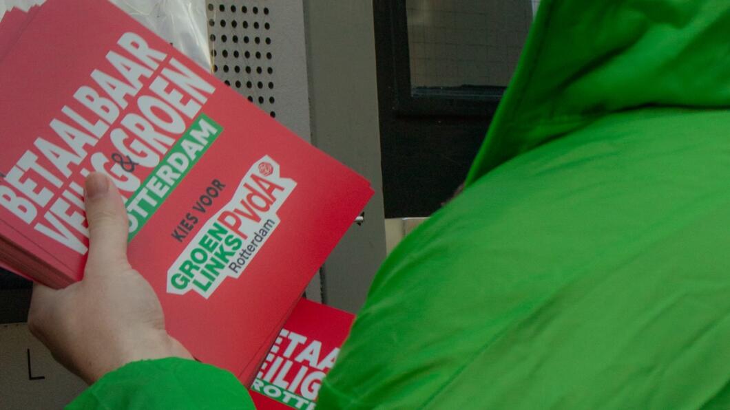 een persoon met een groene jas houdt een stapel flyers vast