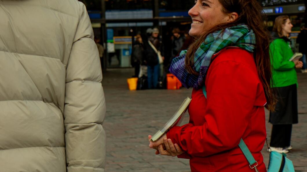 persoon in rode jas staat te flyeren bij het station