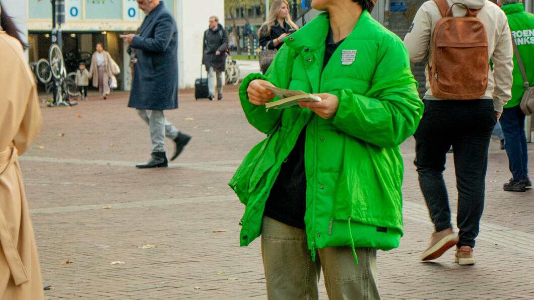 persoon in groene jas staat buiten te flyeren