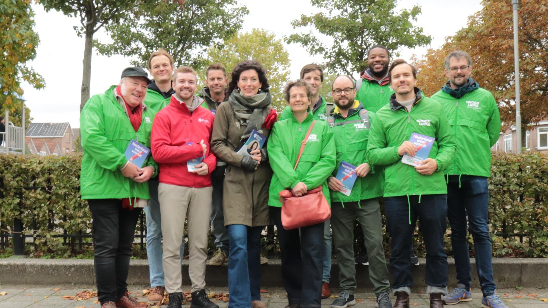 Groep vrijwilligers met groene en rode jasjes met flyers in hun handen. Marleen Haage staat in het midden.