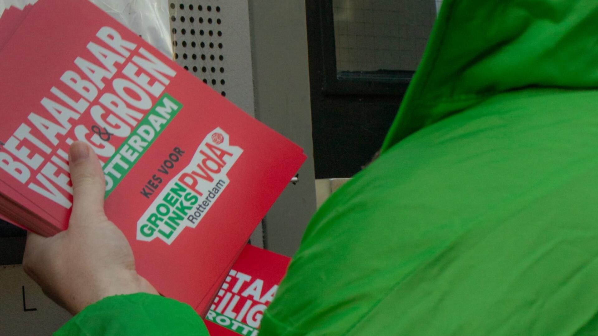 een persoon met een groene jas houdt een stapel flyers vast
