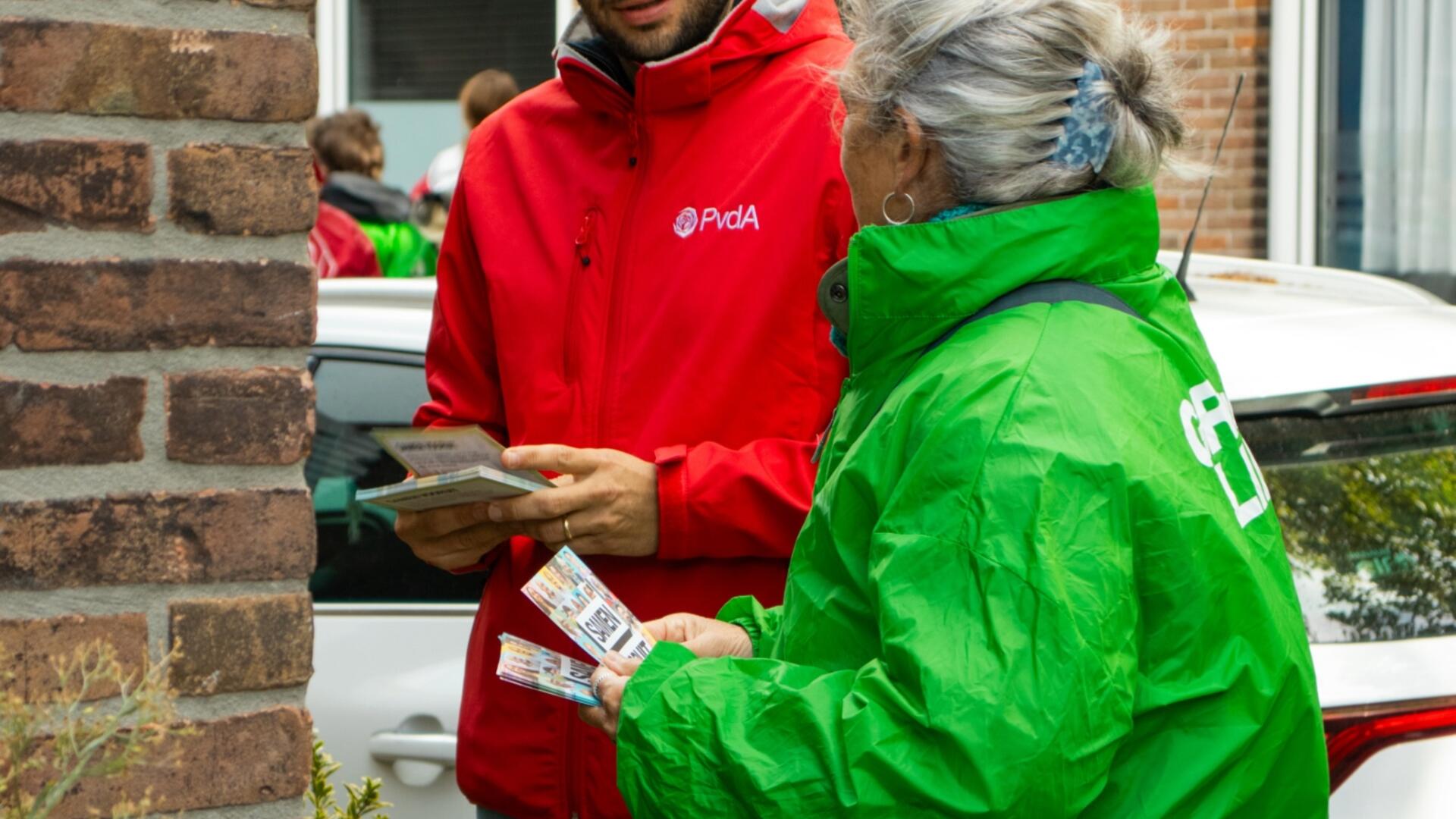 twee mensen met rode en groene jas staan te flyeren