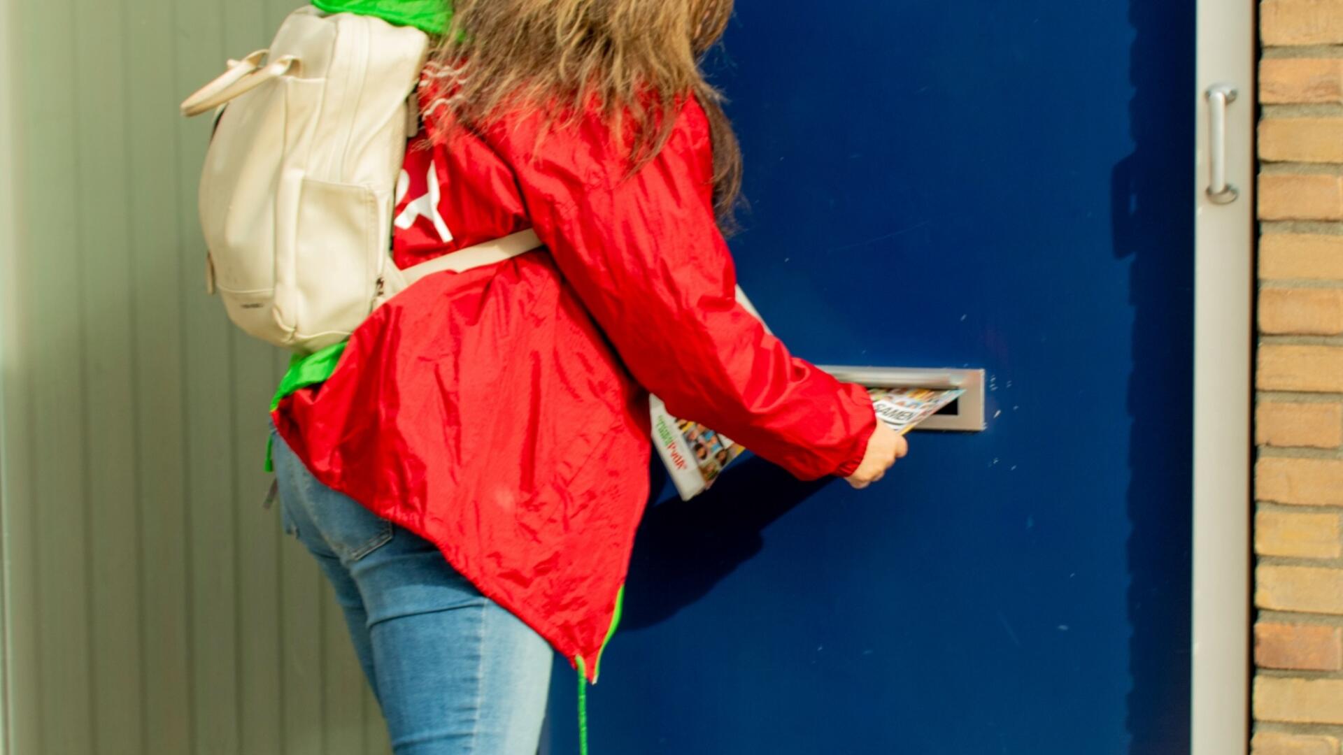 een persoon in rode jas doet een flyer door de brievenbus
