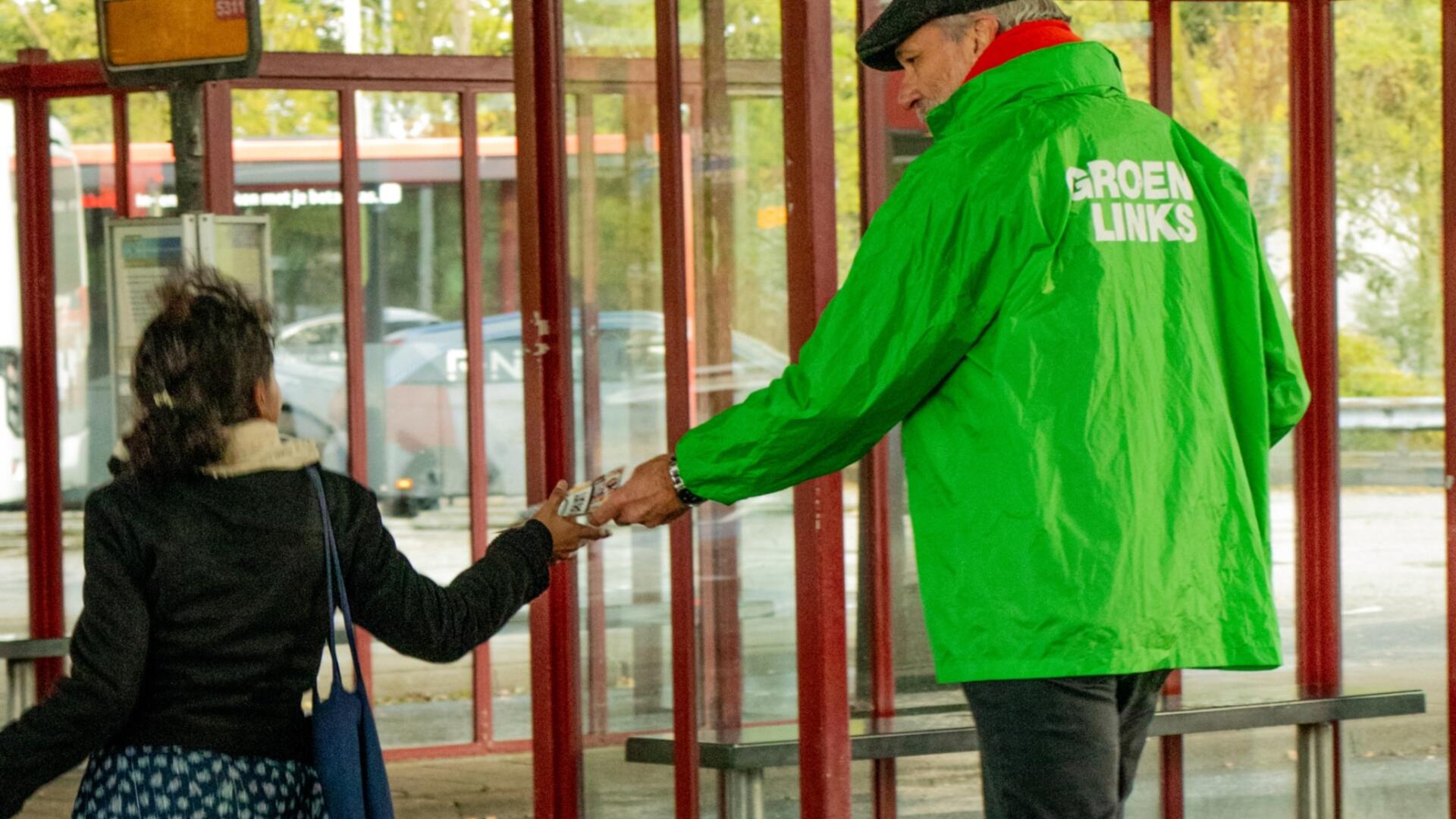 persoon in groene jas deelt flyer uit